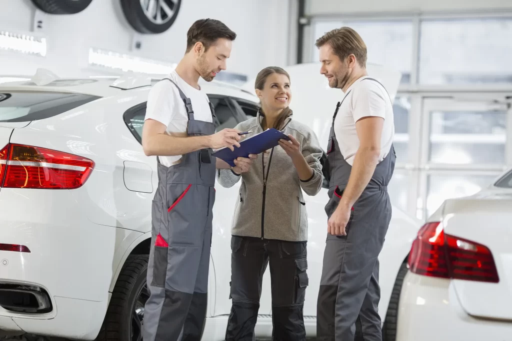 Two car mechanics explaining auto repair and maintenance to a client.
