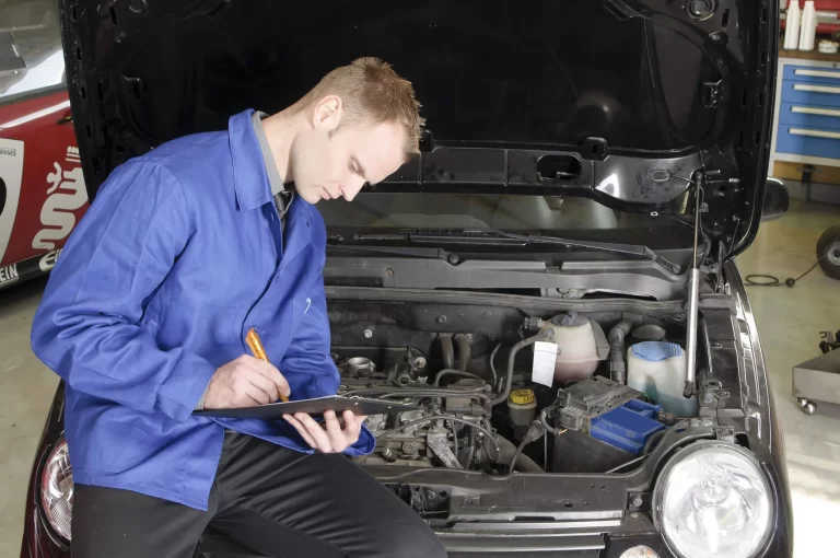 An auto mechanic checking the engine compartment of a car.