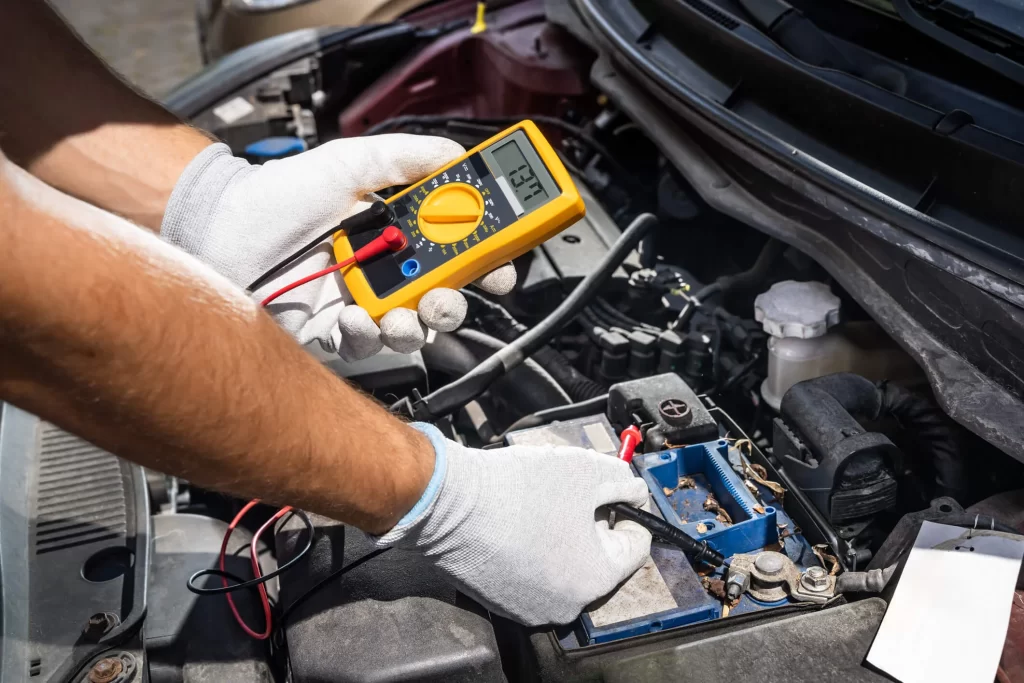 A mechanic holding a voltmeter and checking a car's battery.