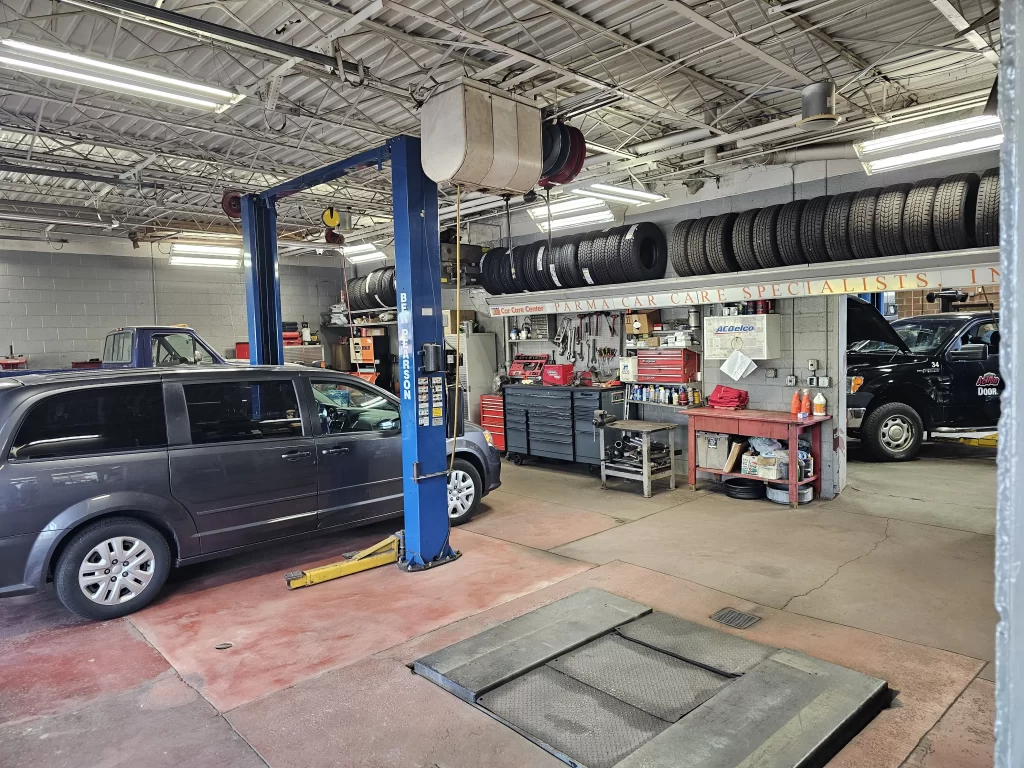 A full shot of an auto repair shop garage with autos on a car lift and tires on racks.