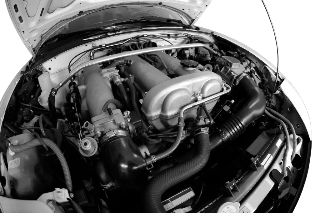 A black-and-white photo of car parts under the hood.